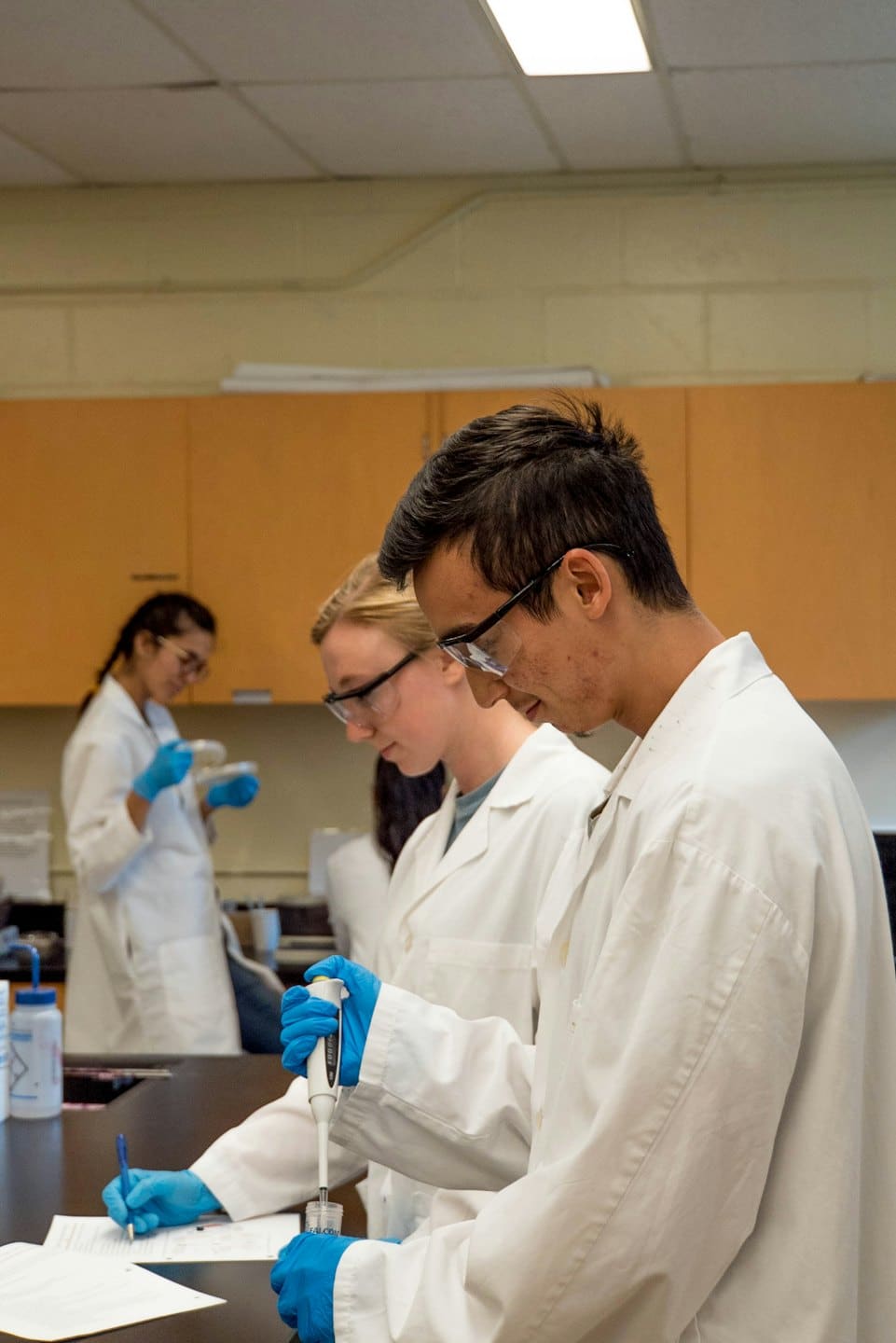 Three scientists in lab coats conduct experiments in a laboratory.